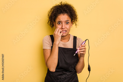 Photography Young African american manicurist woman holding an electric file drill isolated biting fingernails, nervous and very anxious