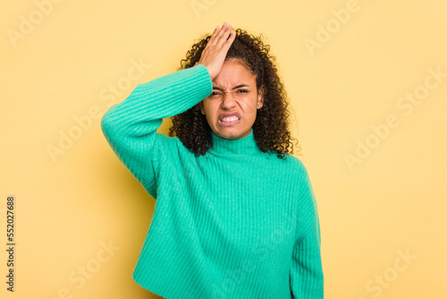 Young Brazilian curly hair cute woman isolated on yellow background forgetting something, slapping forehead with palm and closing eyes. © Asier