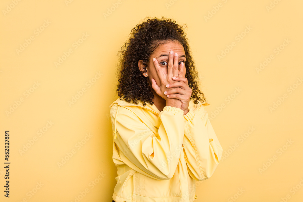 Young Brazilian curly hair cute woman isolated on yellow background blink through fingers frightened and nervous. Young Brazilian curly hair cute woman isolated on yellow background blink through fingers frightened and nervous.