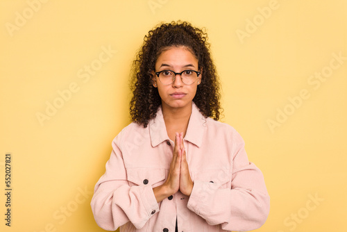 Billede på lærred Young Brazilian curly hair cute woman isolated on yellow background praying, showing devotion, religious person looking for divine inspiration