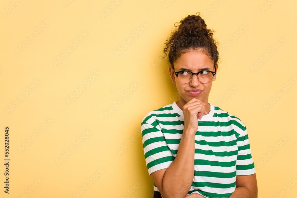 Young Brazilian curly hair cute woman isolated on yellow background looking sideways with doubtful and skeptical expression. Young Brazilian curly hair cute woman isolated on yellow background looking sideways with doubtful and skeptical expression.