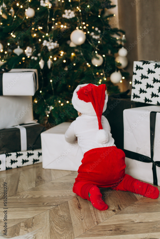 Obraz premium a small child looks at gifts under the tree in a Santa costume