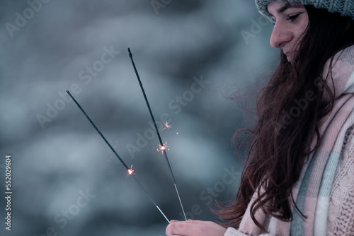 Happy new year,portrait of a happy beautiful brunette girl in the snow, with winter hat and warm gloves in the sunny winter day,Outdoor waist up portrait,girl holding sparklers, New Year's Eve