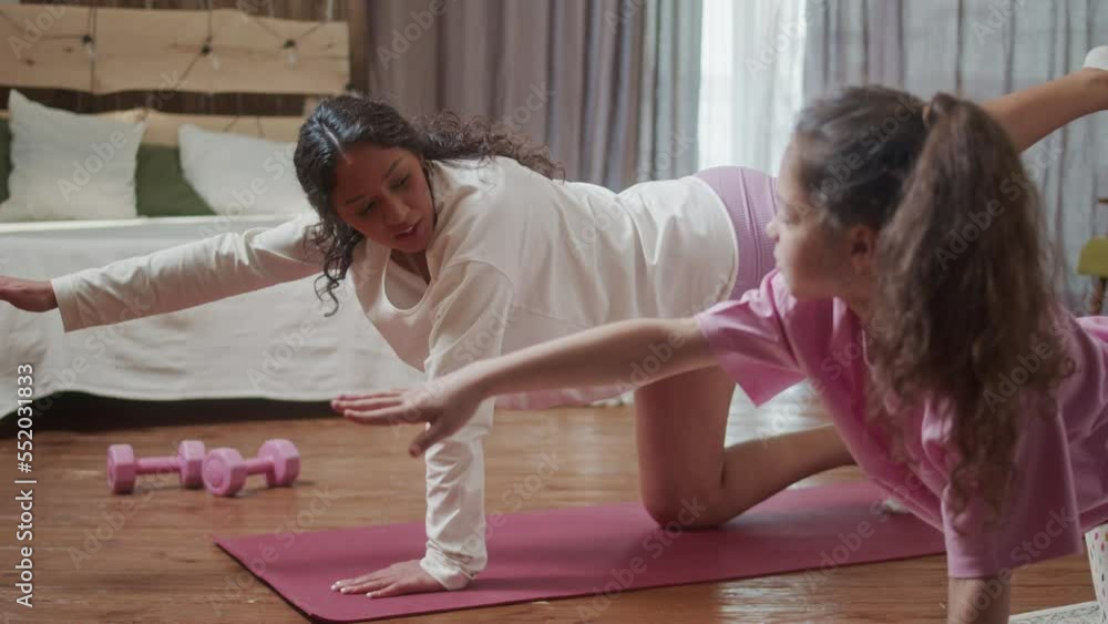 Young Hispanic Woman teach doing stretching exercises training her little cute daughter, sit floor in cozy living room perform. Happy activity in family concept. Young Hispanic Woman teach doing stretching exercises training her little cute daughter, sit floor in cozy living room perform. Happy activity in family concept.