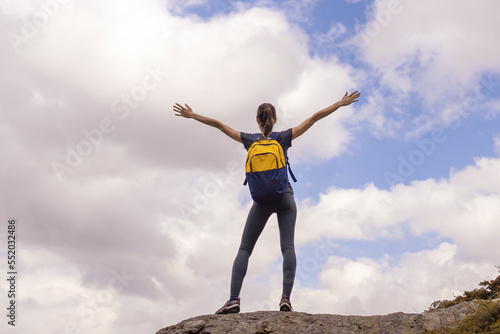 Woman traveller with arms raised on top of mountain looking at view. medium shot
