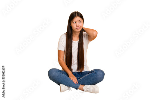 Young asian woman sitting on the floor cutout isolated touching back of head, thinking and making a choice.