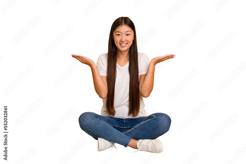 Young asian woman sitting on the floor cutout isolated makes scale with arms, feels happy and confident. Young asian woman sitting on the floor cutout isolated makes scale with arms, feels happy and confident.