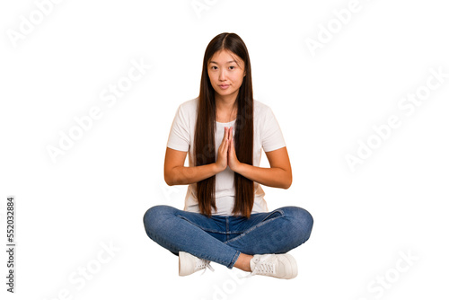 Young asian woman sitting on the floor cutout isolated praying, showing devotion, religious person looking for divine inspiration.