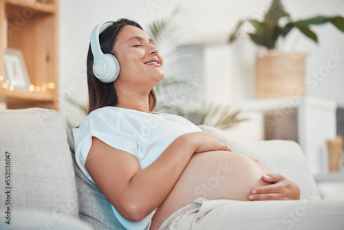 Music, headphones and pregnant woman relax on sofa in home living room streaming radio or podcast. Pregnancy, meditation and female from Canada on couch listening to song, audio or sound in house. photo