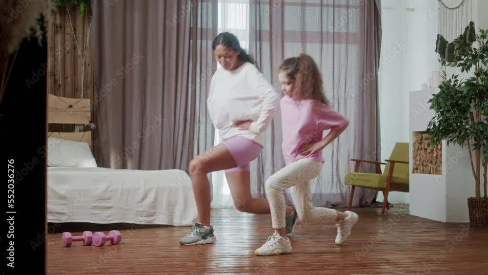 Young Hispanic Woman teach doing stretching exercises training her little cute daughter in cozy living room perform. Happy activity in family concept. Young Hispanic Woman teach doing stretching exercises training her little cute daughter in cozy living room perform. Happy activity in family concept.