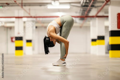 Sportswoman is bending and stretching her body in underground garage.