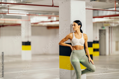A sportswoman is leaning on the pillar in underground garage and posing.