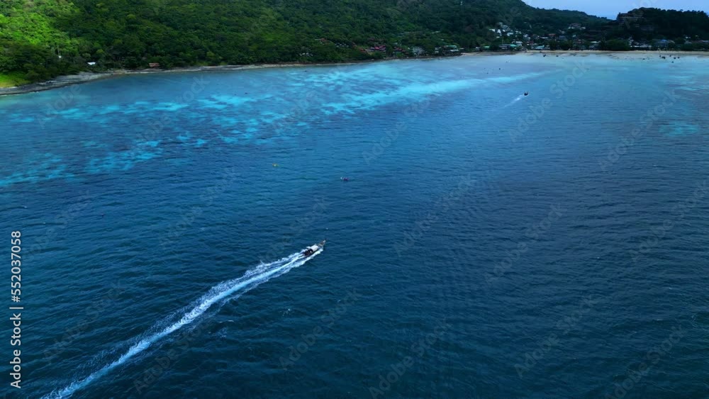 Long Tail Boat at the coast of Koh Phi Phi Island in southern Thailand, Krabi, Phuket. Green and rocky cliffs with trees and jungle. 4K drone shot.