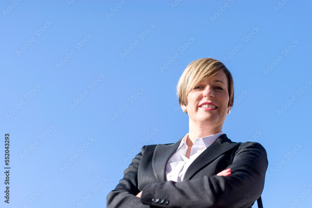 Low angle portrait of a young businesswoman standing outdoors and crossing her arms. Low-angle shot Low angle portrait of a young businesswoman standing outdoors and crossing her arms. Low-angle shot