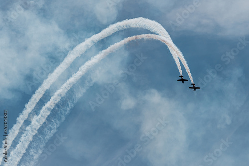 two small planes fly in parallel describing a white trajectory over the blue sky. condensation trails. concept synchronization and partnership.