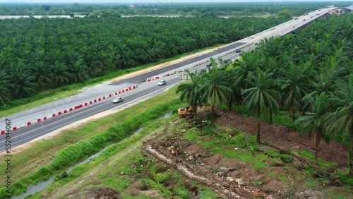 Aerial drone fly around sabrang estate sime darby plantation, thriving palm tree farm in teluk intan along side E32 west coast expressway, interstate highway, excavator removing the grove. photo