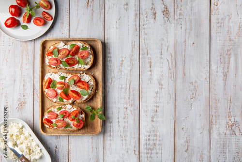 Sandwich with cottage cheese, tomatoes and basil on white wooden background. Traditional Italian bruschetta. Healthy savory feta and tomato toast. Top view. Copy space.