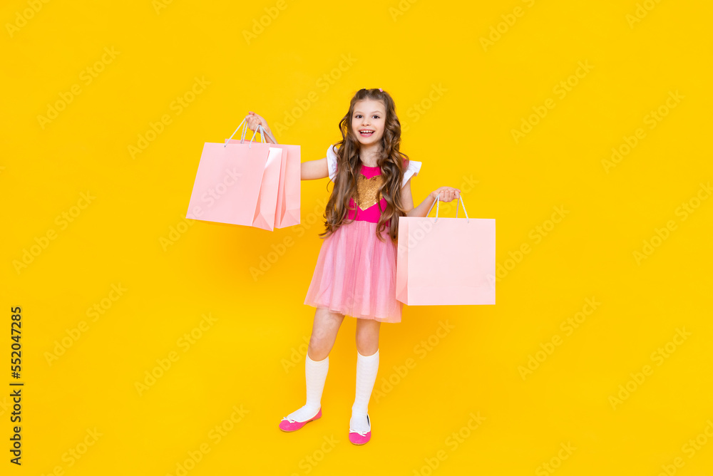 Fototapeta premium New purchases for the summer, a little girl returns from the store with large bags of things. A child in a pink dress with shopping bags on an isolated background.