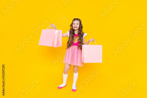 New purchases for the summer, a little girl returns from the store with large bags of things. A child in a pink dress with shopping bags on an isolated background.
