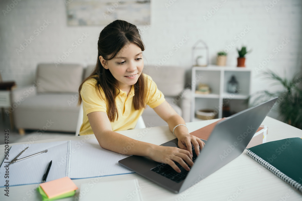 smiling brunette girl typing on laptop near notebook on table at home smiling brunette girl typing on laptop near notebook on table at home