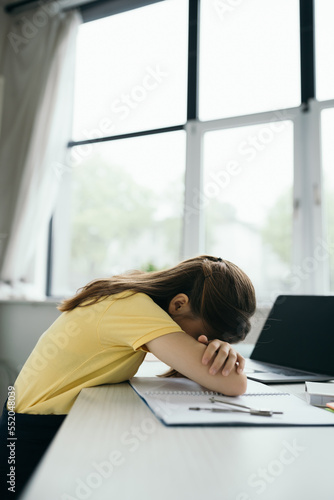 side view of exhausted schoolgirl sleeping near laptop with blank screen on table