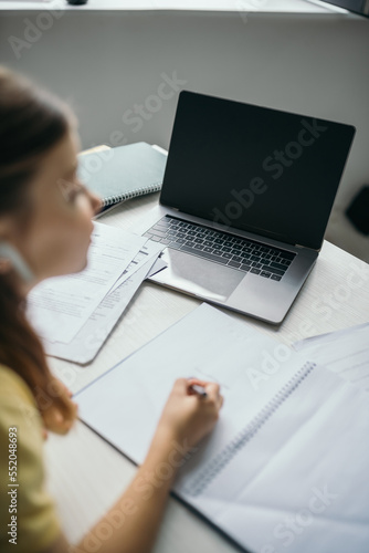 high angle view of blurred girl studying near laptop with blank screen at home