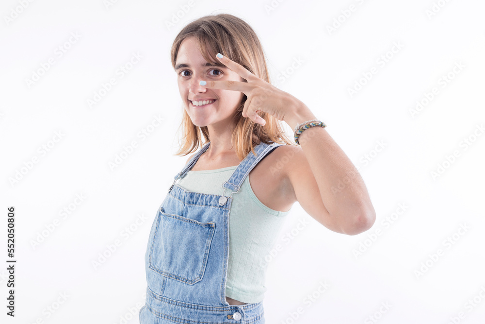 cheerful redhead young woman model showing victory sign with fingers, eyes open on white background. cheerful redhead young woman model showing victory sign with fingers, eyes open on white background.