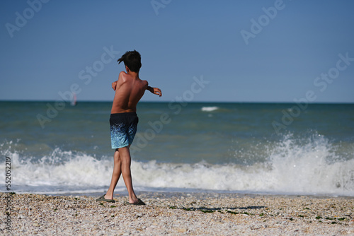 Back of boy throw pebbles into the sea in beach Porto Sant Elpidio, Italy. photo