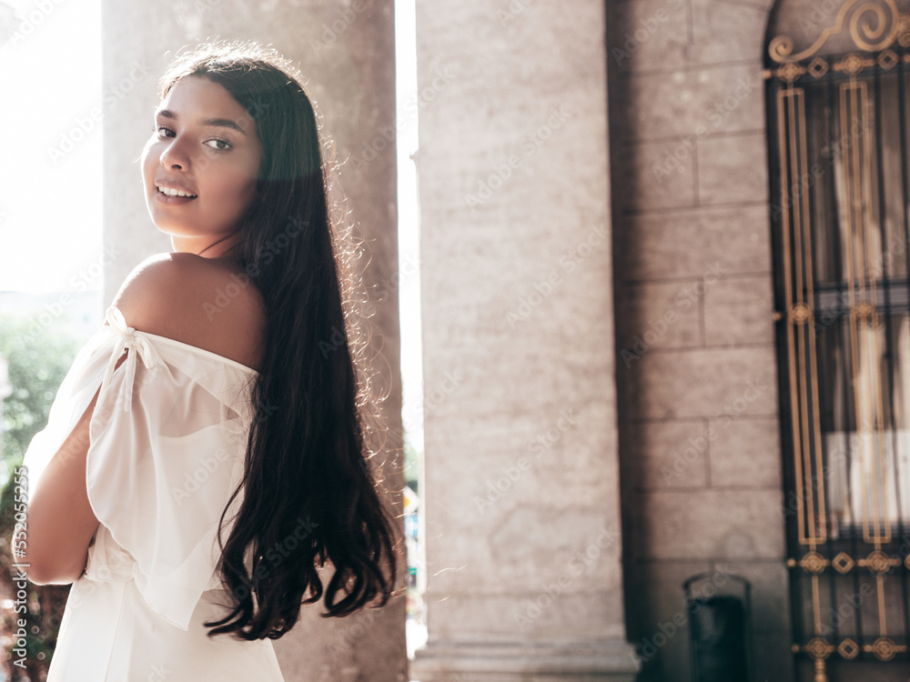 Young beautiful smiling hipster woman in white dress. Sexy carefree model posing on the street background at sunset. Positive female outdoors at warm sunny day. Cheerful and happy. Turns around Young beautiful smiling hipster woman in white dress. Sexy carefree model posing on the street background at sunset. Positive female outdoors at warm sunny day. Cheerful and happy. Turns around