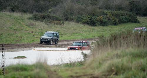 three land rover discovery 4x4 off-road vehicles being driven through deep water and mud in open countryside, Wiltshire UK © Martin