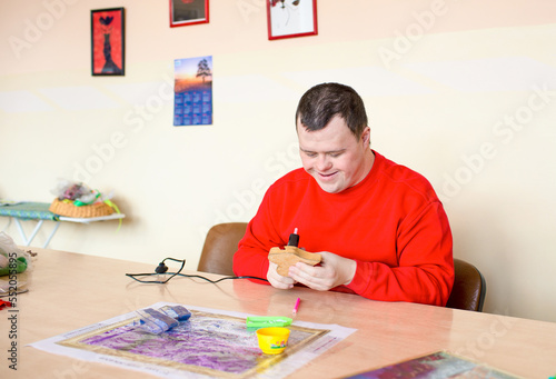 An adult man with a mental disorder syndrome glues paper in the workshop #552055895