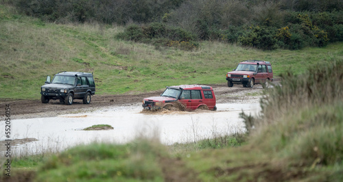 three land rover discovery 4x4 off-road vehicles being driven through deep water and mud in open countryside, Wiltshire UK