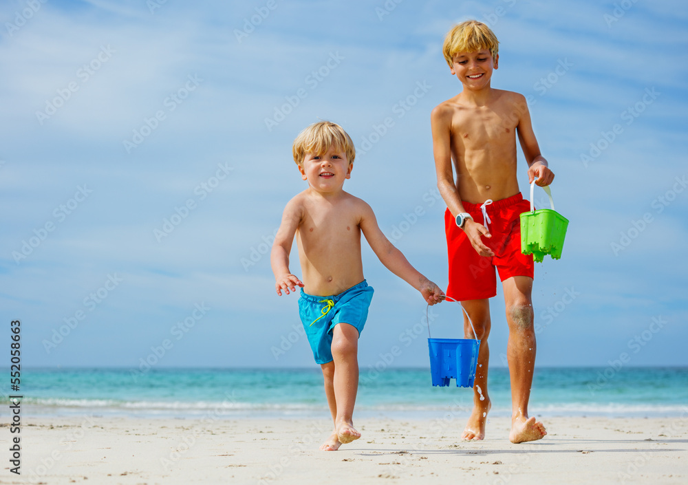 Two happy smiling boys run with water buckets from sea waves