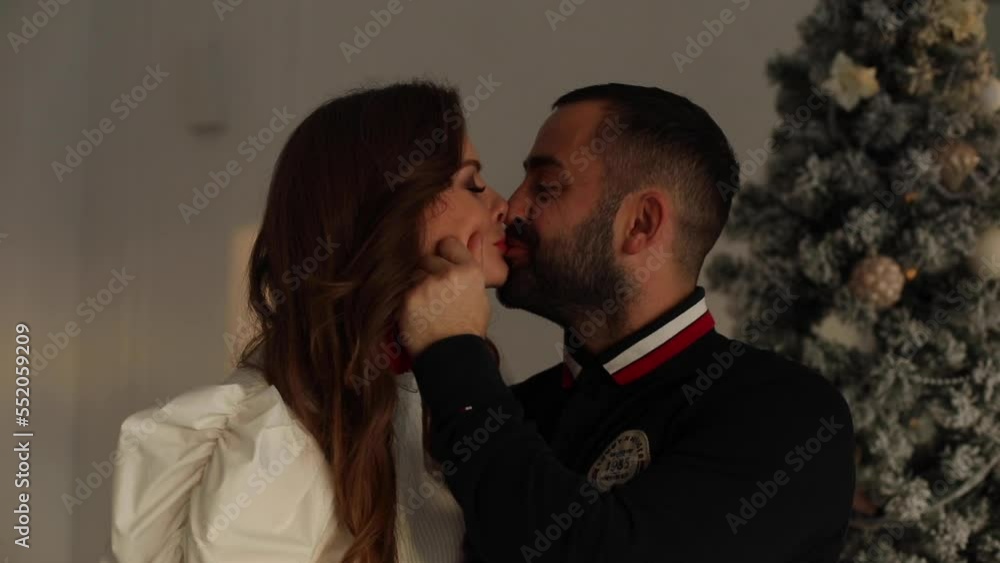 Romantic couple wearing pyjamas smiling and kissing on background of christmas tree on xmas holidays Romantic couple wearing pyjamas smiling and kissing on background of christmas tree on xmas holidays