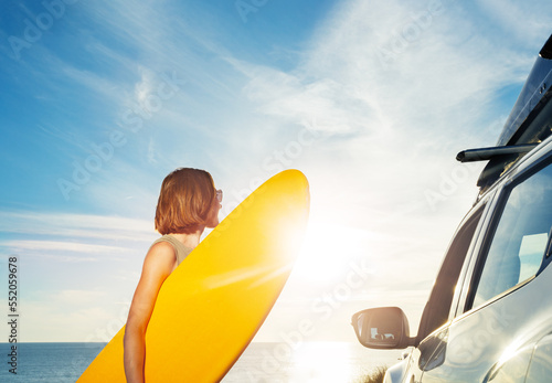 Woman with surf board by the car look on sunset over ocean
