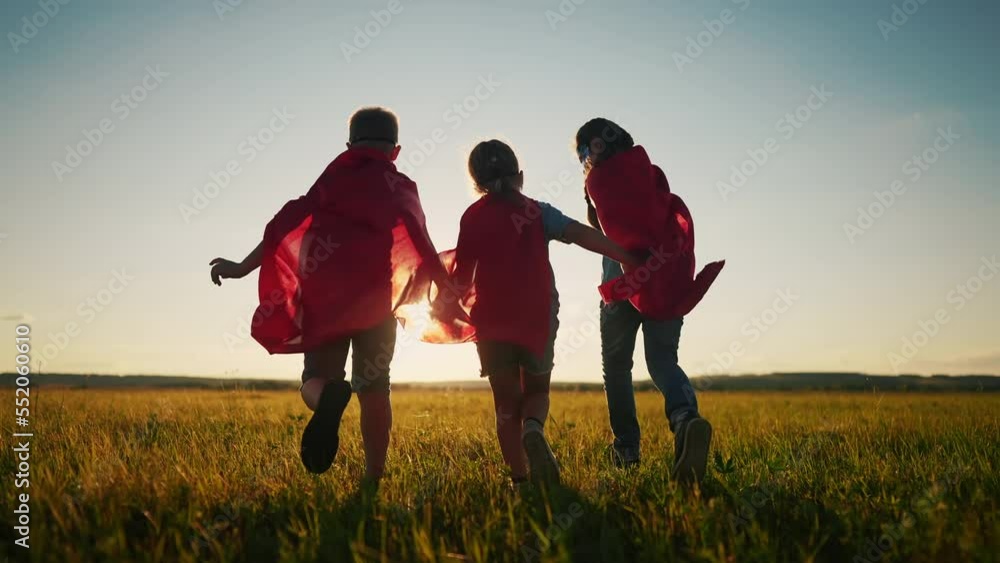 team superhero. a group of children are running across the field in a superhero costume with a silhouette of a red dream cape at sunset. the concept of a happy family childhood. teamwork superhero team superhero. a group of children are running across the field in a superhero costume with a silhouette of a red dream cape at sunset. the concept of a happy family childhood. teamwork superhero