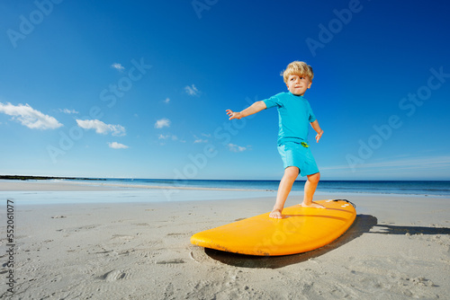 Low angle portrait of blond boy stand on the surfboard at beach