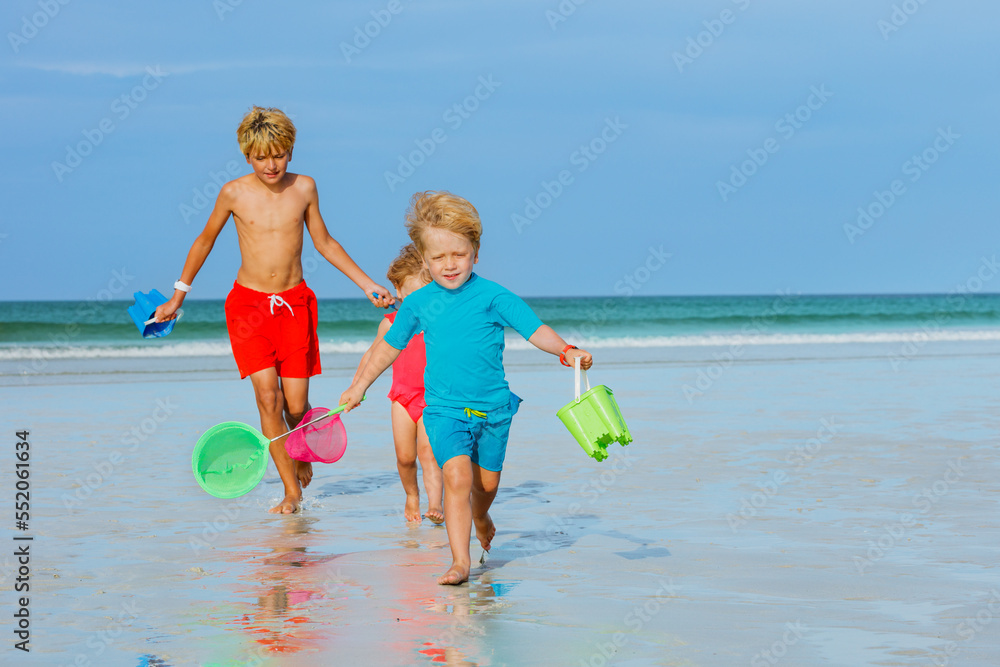 Three kids run on a beach hold buckets and hoop-net catch crabs Three kids run on a beach hold buckets and hoop-net catch crabs