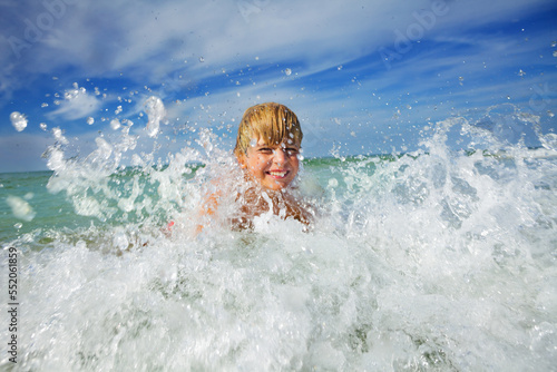 Boy play in ocean wave with water splashes during vacations