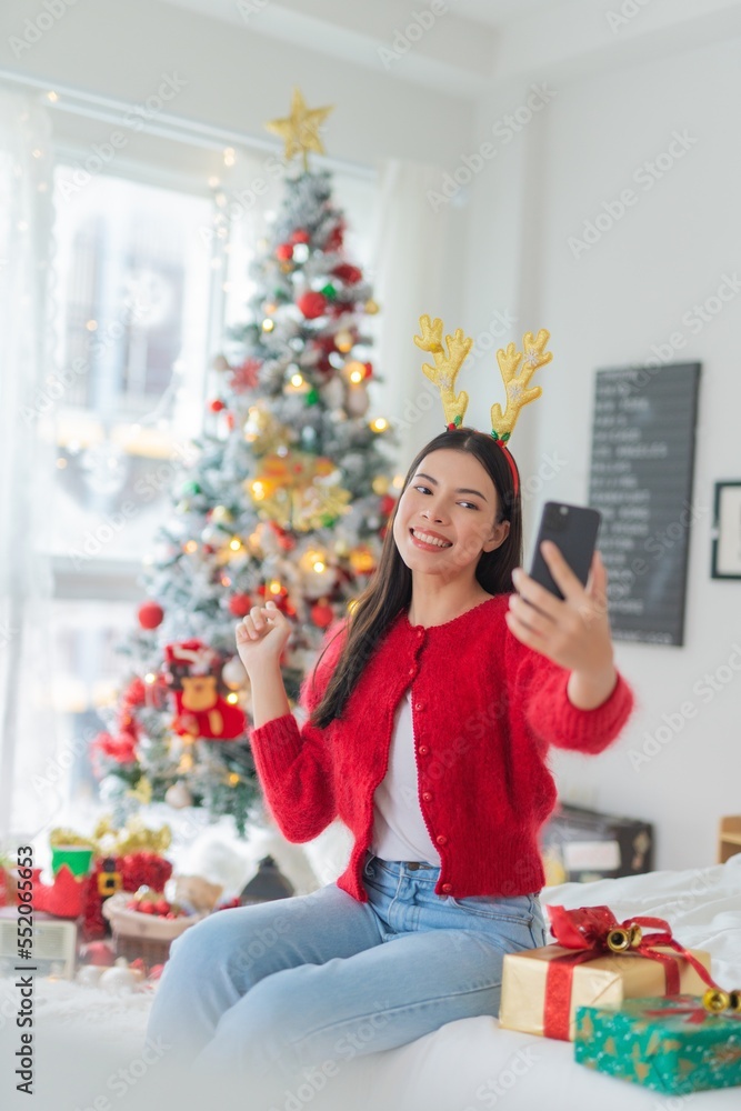 Young asian woman wearing reindeer headband selfie in front a big Christmas tree Young asian woman wearing reindeer headband selfie in front a big Christmas tree