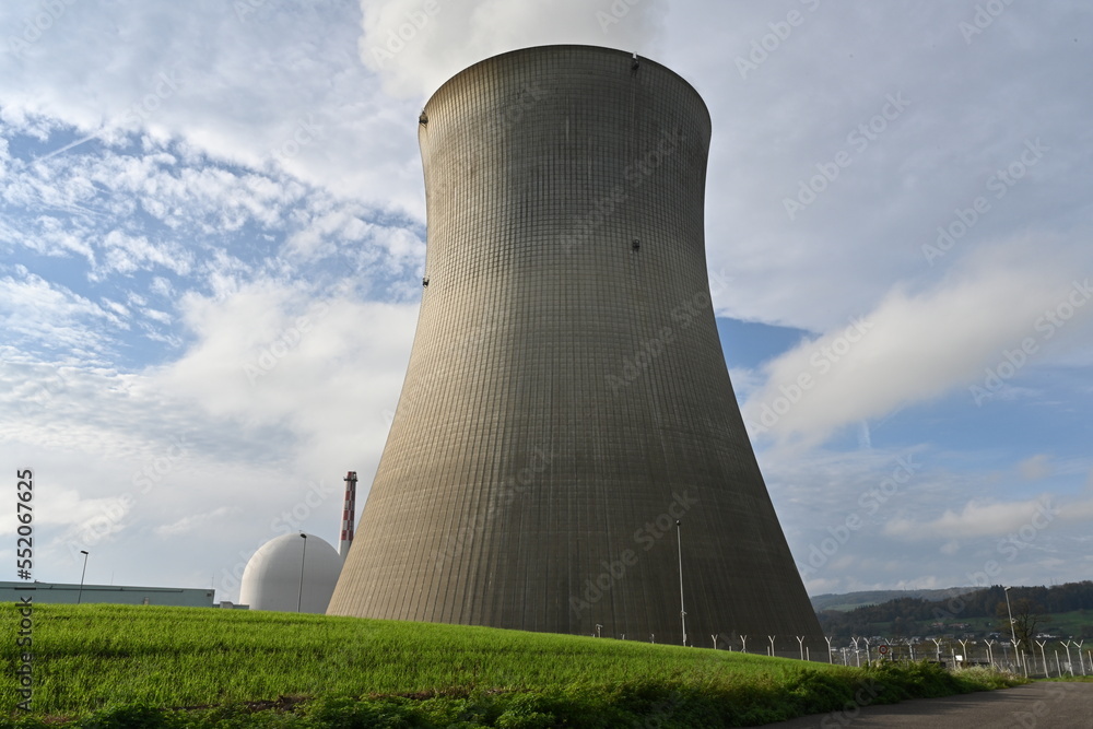 Huge cooling tower of a nuclear power plant observed from vicinity. Behind is white structure covering reactor and chimney. In foreground is green field and fence. Huge cooling tower of a nuclear power plant observed from vicinity. Behind is white structure covering reactor and chimney. In foreground is green field and fence.