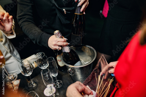 Bachelorette party and table with alcohol, champagne bottles, glasses and female hands. Open a bottle of booze. Holiday
