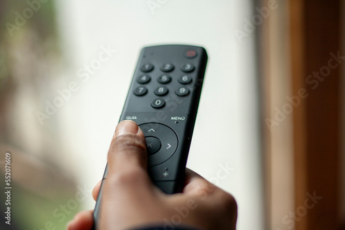 hand directing a television remote where you can see the different keyboard controls, with a blurred background photo