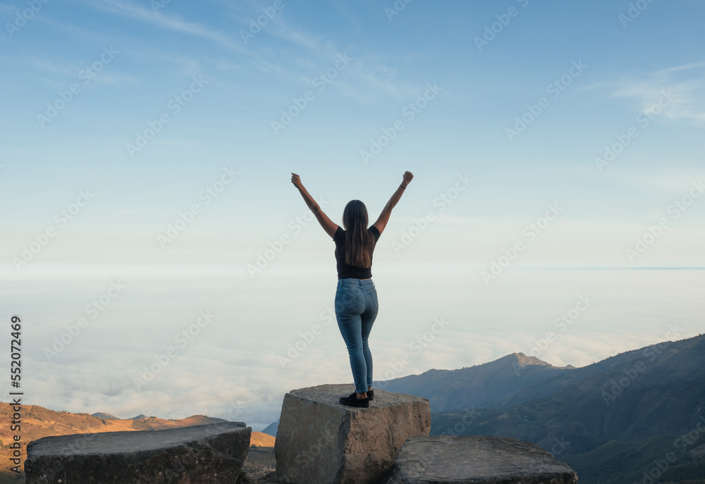 woman standing on a rock with a landscape full of sky and mountains, in the Ecuadorian highlands, she raises her hands as a sign of success for having achieved her goals. woman standing on a rock with a landscape full of sky and mountains, in the Ecuadorian highlands, she raises her hands as a sign of success for having achieved her goals.