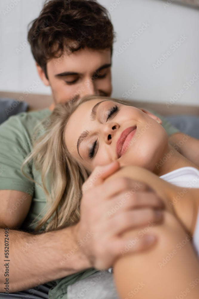 Blurred man hugging joyful blonde girlfriend on bed in morning. Blurred man hugging joyful blonde girlfriend on bed in morning.