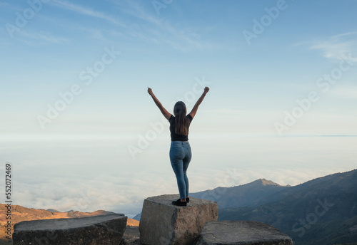 woman standing on a rock with a landscape full of sky and mountains, in the Ecuadorian highlands, she raises her hands as a sign of success for having achieved her goals.