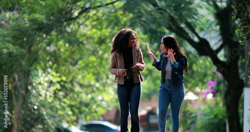 Obraz na plátně Two diverse young women laughing together while walking outside in street