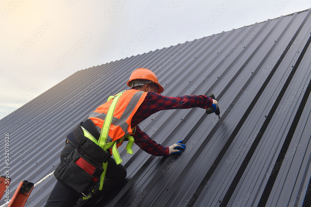 background Roofer worker in protective uniform wear and gloves,Roofing tools,installing new roofs under construction,Electric drill used on new roofs with metal sheet.