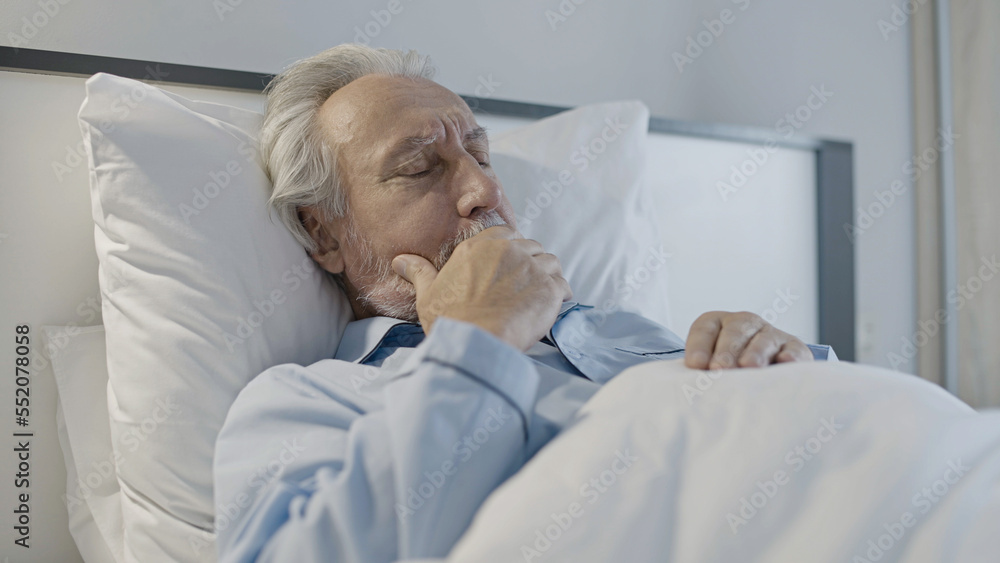 Obraz premium Old man coughing, lying in bed, shortness of breath, symptom of bronchitis