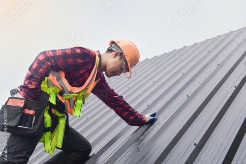 Roofer worker in protective uniform wear and gloves,Roofing tools,installing new roofs under construction,Electric drill used on new roofs with metal sheet. photo